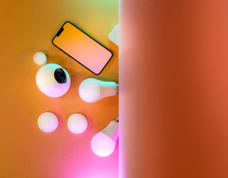 Equipamentos Essenciais para Manter a Casa Segura Light Bulbs Next to Camera and Smartphone on Pastel Background