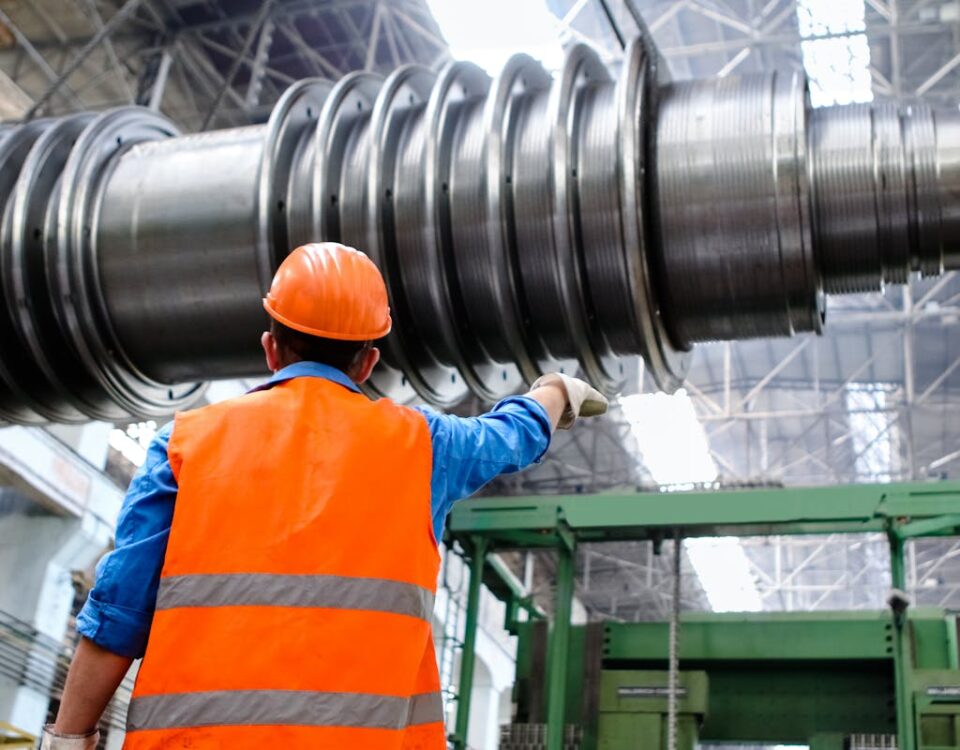 Dispositivos inteligentes para monitorar encanamentos Engineer in high visibility vest and hard hat inspecting large machinery in factory setting.