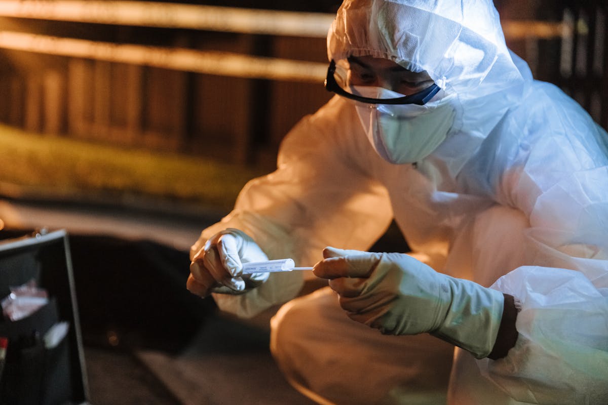 A forensic investigator in protective gear collects evidence outdoors at night.