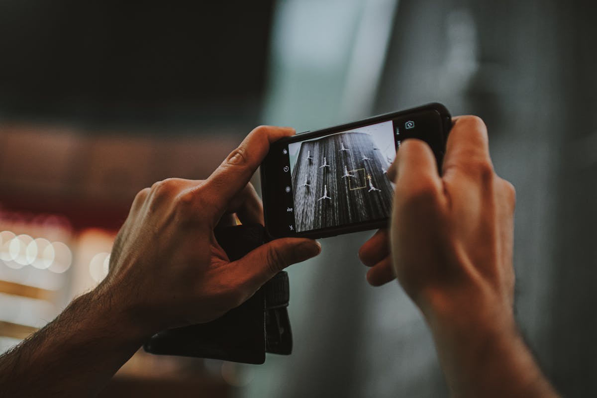 Equipamentos essenciais para fotos de qualidade no Instagram Hands holding a smartphone capturing an indoor scene in Dubai, featuring a modern lifestyle.
