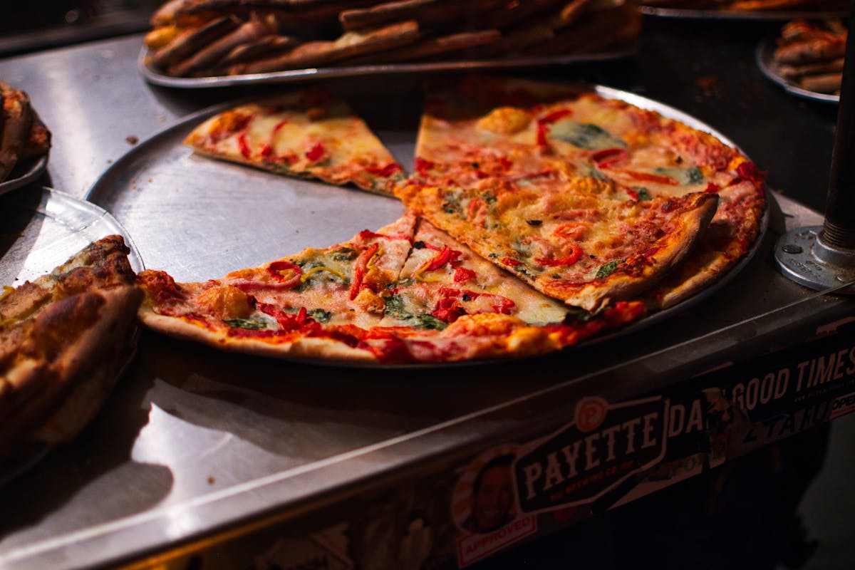 A mouth-watering view of vegetarian pizza slices with toppings on a metal tray, ready to serve.