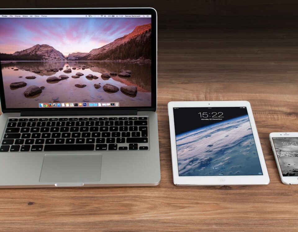 Gadgets essenciais para monitorar sites remotamente Modern workspace showcasing Apple laptop, tablet, and smartphone on a wooden desk.