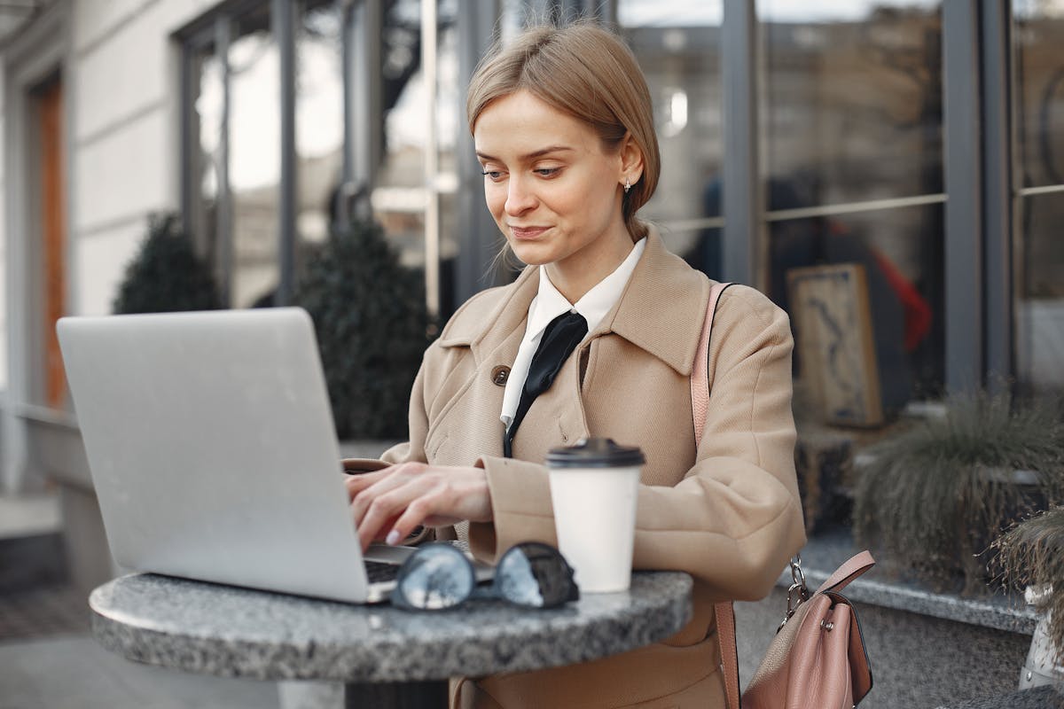 Confident businesswoman using laptop at outdoor café table, enjoying coffee.