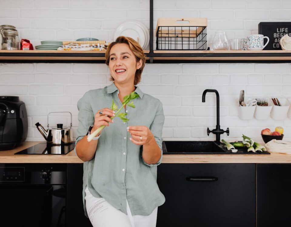 Smiling woman with vegetables in a stylish kitchen showcasing modern interior design.