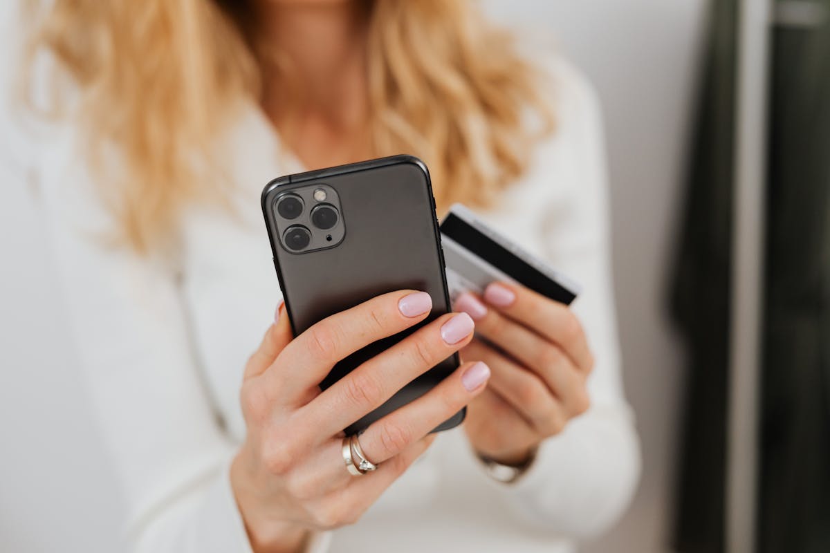 Close-up of woman holding smartphone and credit card for online transaction indoors.
