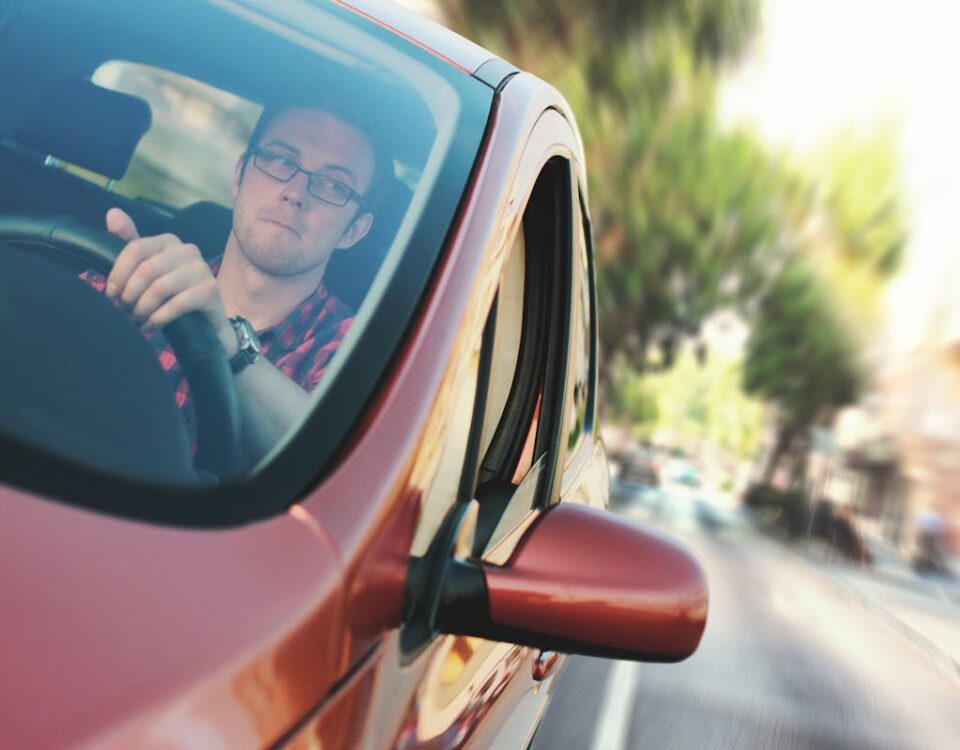 Gadgets úteis para novos motoristas A man driving fast through a city street in a red car, showcasing motion and focus.