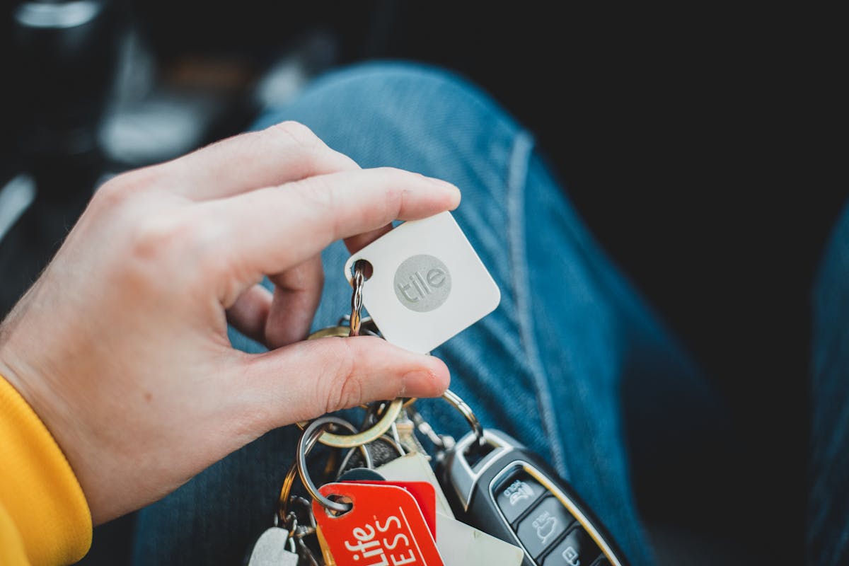 Gadgets que ajudam na redução do seguro do carro A close-up of a hand holding a set of car keys with various keychains and tags. Indoor setting.