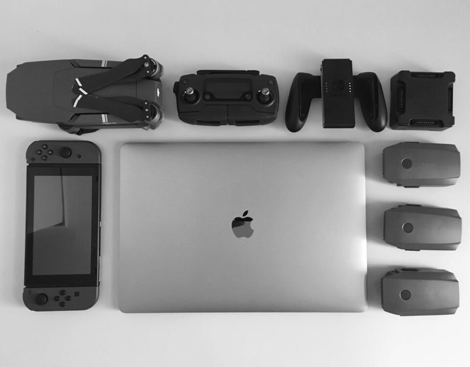 A black and white flat lay of various modern tech gadgets including a laptop, drone, and gaming device.