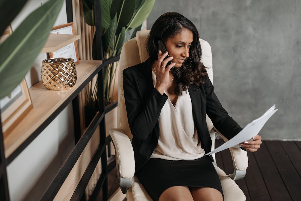 Equipamentos que facilitam a rotina de um advogado criminalista Businesswoman reviews documents while talking on phone in modern office.