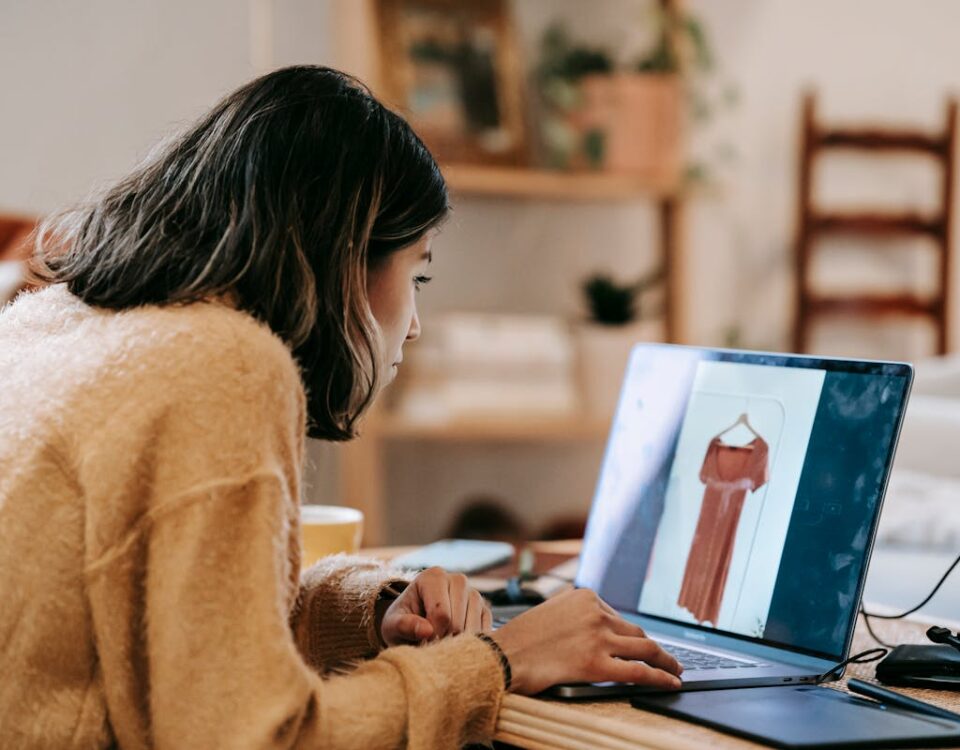 Profissões para trabalho autônomo Young woman using laptop to browse for clothes at home, focusing on an orange dress.