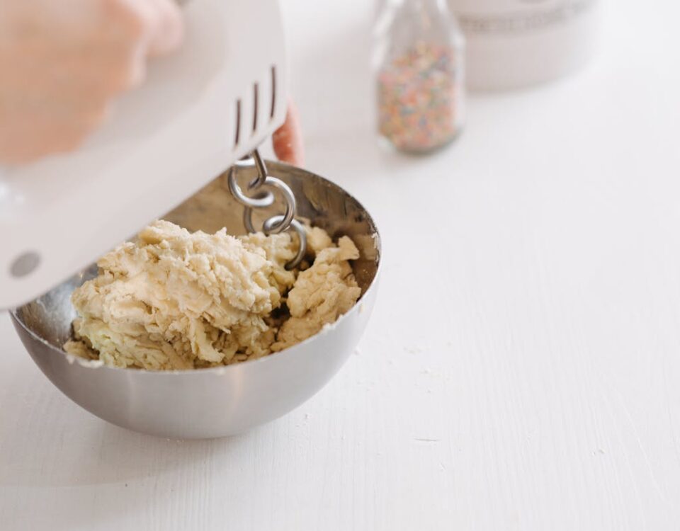 Close-up of dough being mixed in a stainless steel bowl with an electric mixer.