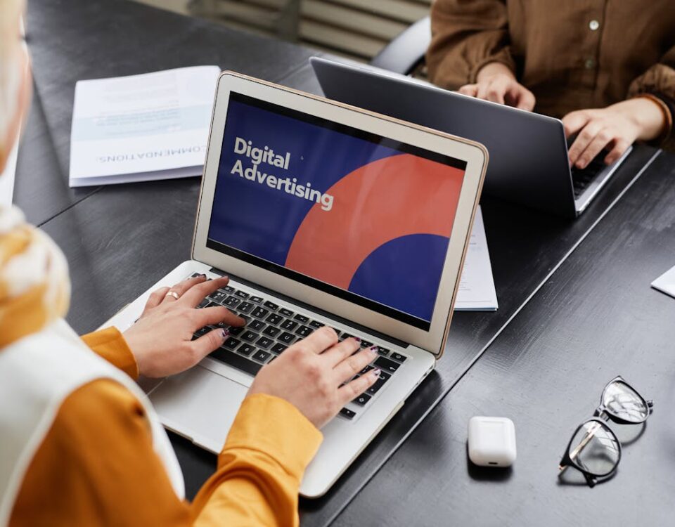 Dispositivos inovadores usados por agências criativas Two professionals work on laptops focusing on digital advertising in an office setting.