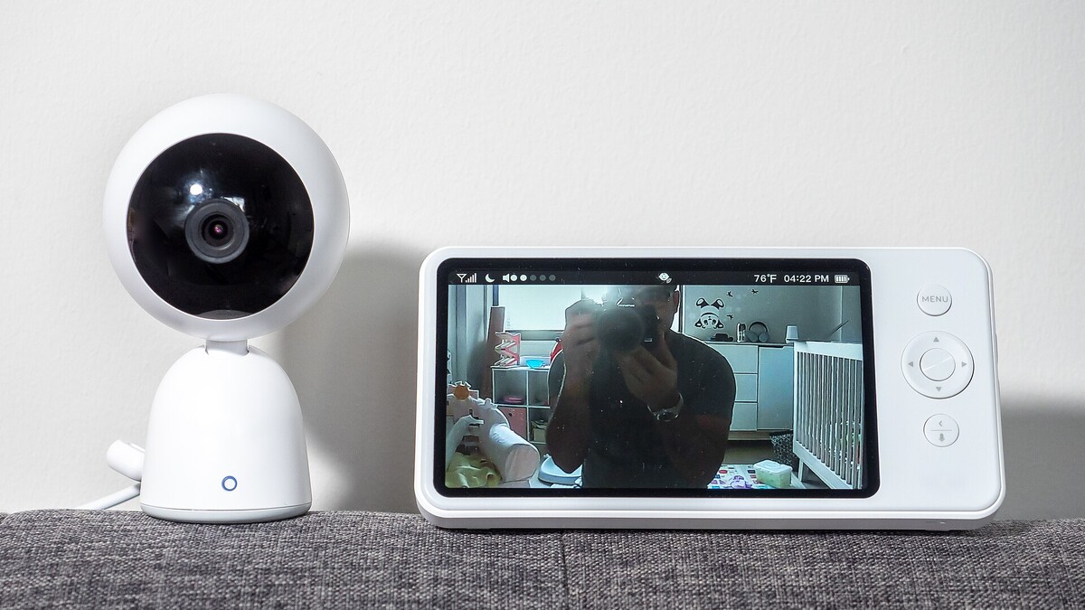 Brinquedo com IA: como checar microfone, Wi-Fi e selo da Anatel Câmera conectada branca ao lado de uma tela que exibe a imagem de um quarto