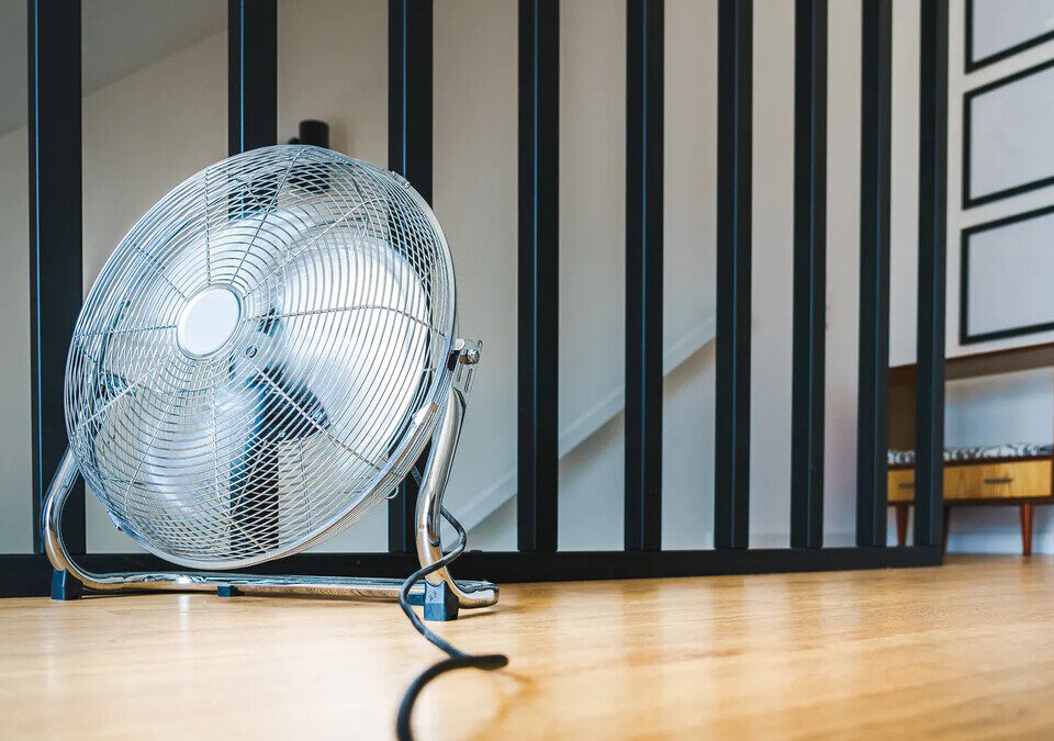Ventilador de piso cromado sobre chão de madeira em sala clara
