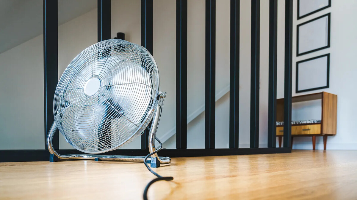 Ventilador de piso cromado sobre chão de madeira em sala clara
