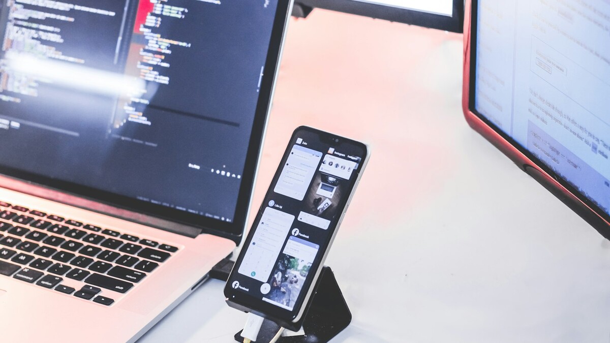 Por que o link do WhatsApp abre no navegador e não no aplicativo? Celular apoiado em suporte ao lado de notebook aberto com código na tela